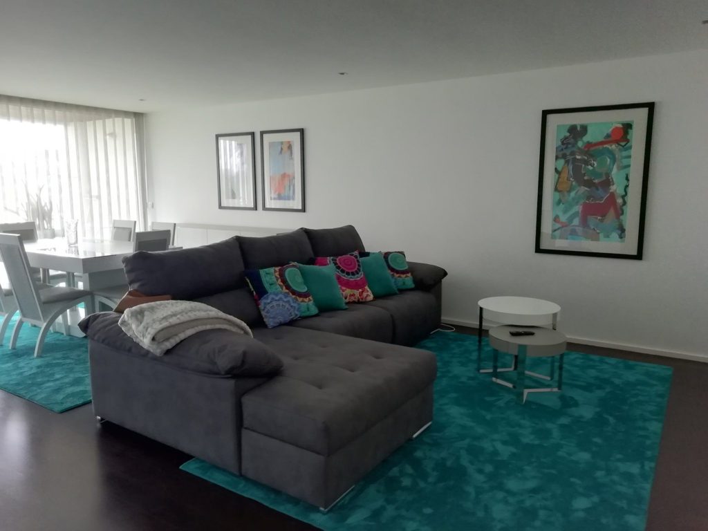 Sala com sofá de canto cinzento, almofadas coloridas e tapete verde-água