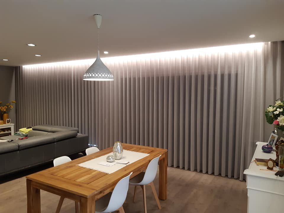 Sala de jantar com cortinas de onda perfeita em cinzento e iluminação embutida no teto