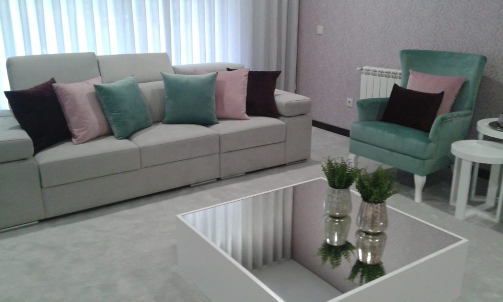 Sala com cadeirão estofado em verde-água e sofá com almofadas em tons de rosa e verde