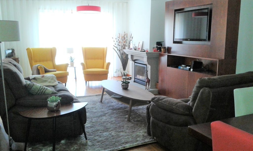 Sala de estar com cadeirões amarelos, sofás cinzentos e lareira